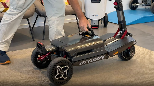 A person folding a compact ATTO Sport mobility scooter by hand in the Movinglife showroom.